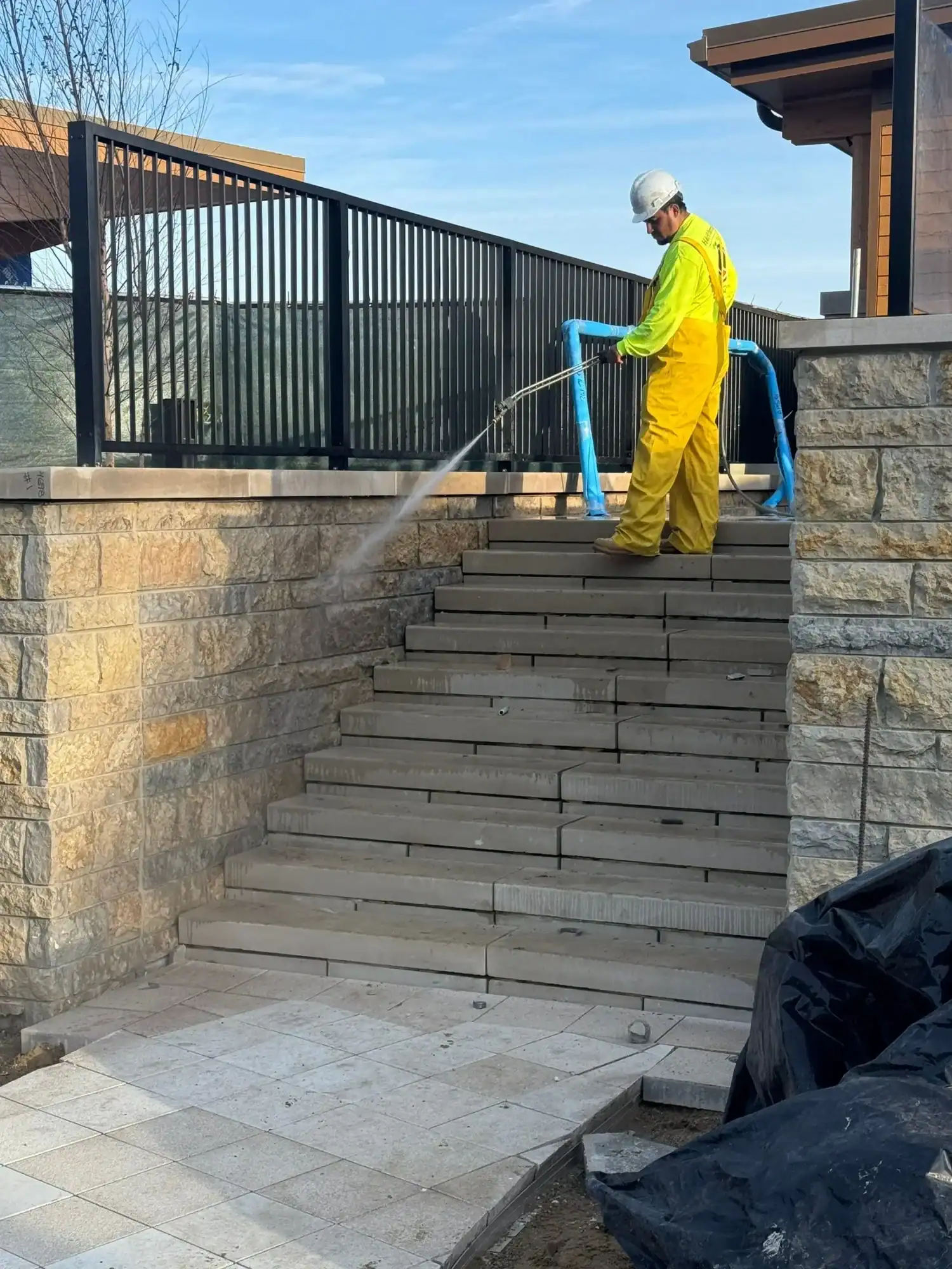 Commercial Pressure Washing Service Worker in yellow protective suit pressure washing dark composite deck stairs and black metal railing in commercial exterior.