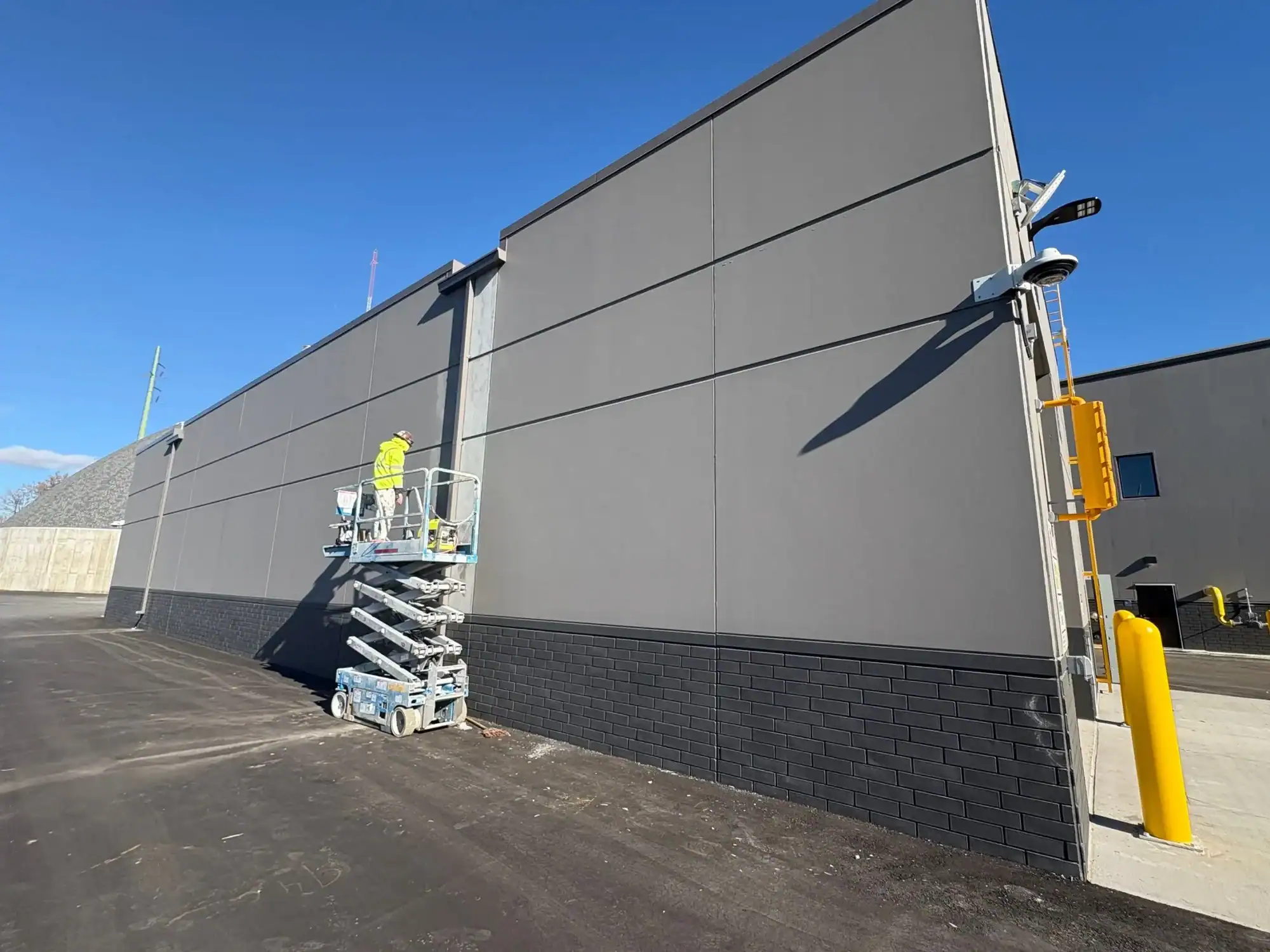 Commercial Building Exterior Painting Gray and black painted commercial building exterior with worker on lift applying finish coating in Grand Rapids, MI.