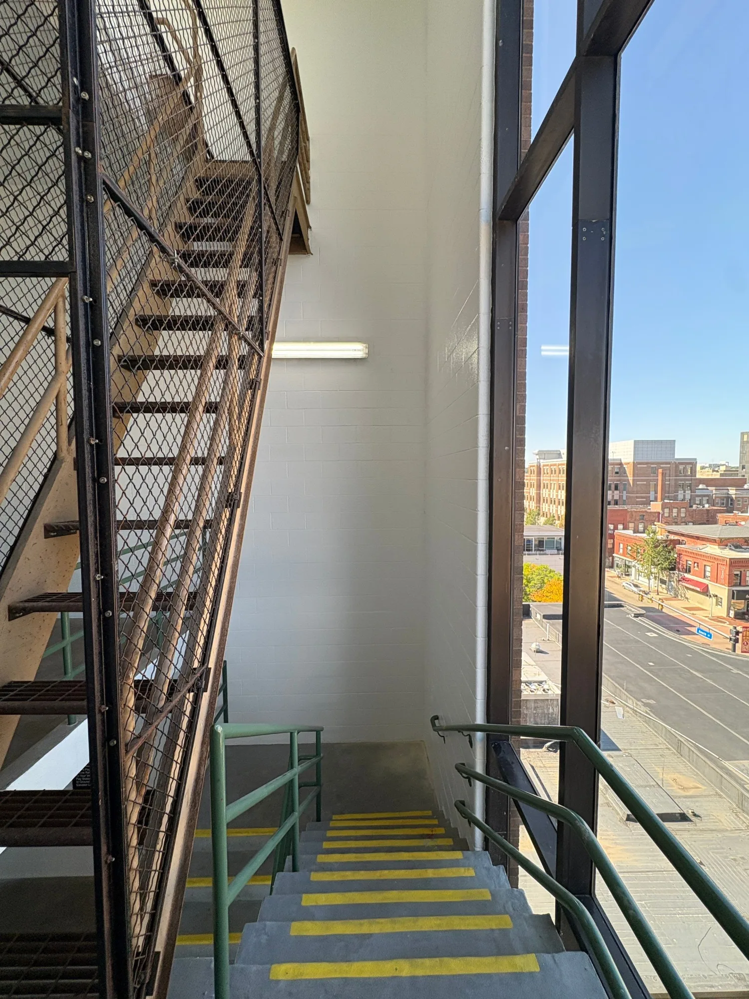 Commercial Stairwell Painting Light gray-painted commercial stairwell wall with black metal safety gate, green railings, yellow stair treads, and city