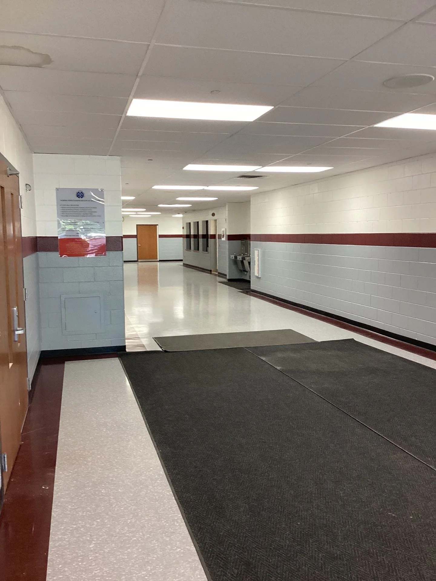 White And Burgundy Commercial Hallway White-painted commercial interior corridor with burgundy stripe accent, polished concrete flooring, charcoal entry mat